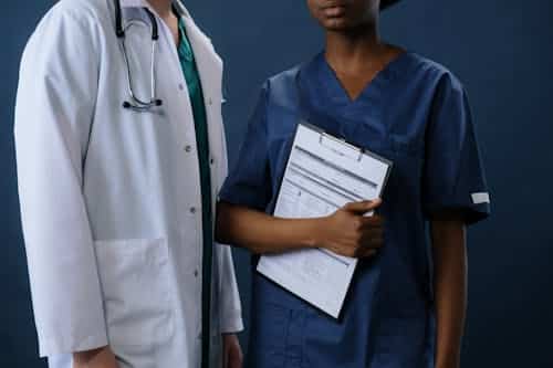 Free Two healthcare professionals in scrubs and lab coat with a clipboard, representing teamwork. Stock Photo